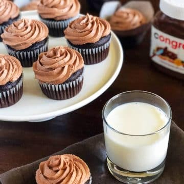 a platter of frosted cupcakes with a jar of nutella and a glass of milk