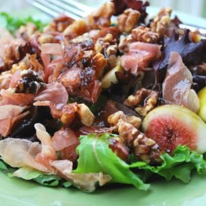 close-up photo of a mixed green salad with prosciutto ham, figs, and nuts