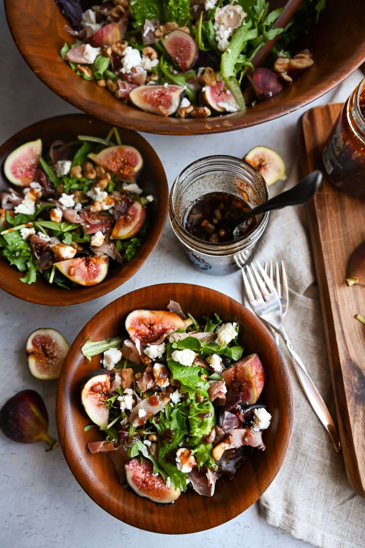 overhead photo of two served bowls of prosciutto salad with a large wood salad bowl and mason jar of homemade dressing