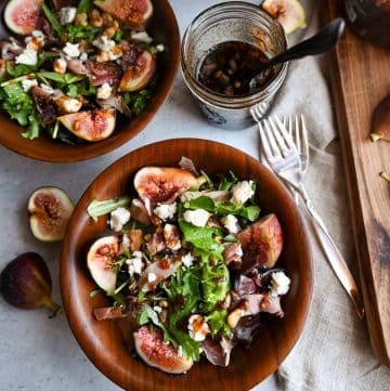 close up photo of proscuitto salad with figs, cheese, and walnuts in a bowl drizzled with dressing with a fork and napkin next to it
