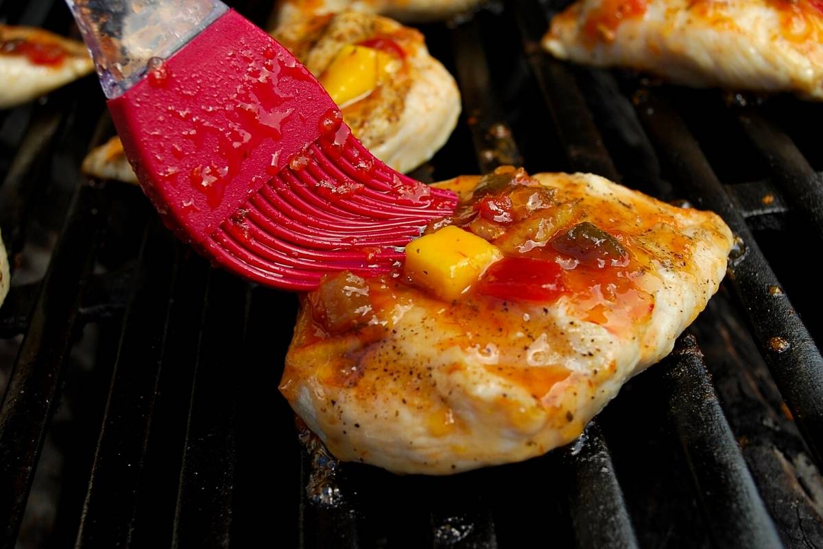 chicken breast on a grill getting basted with mango glaze