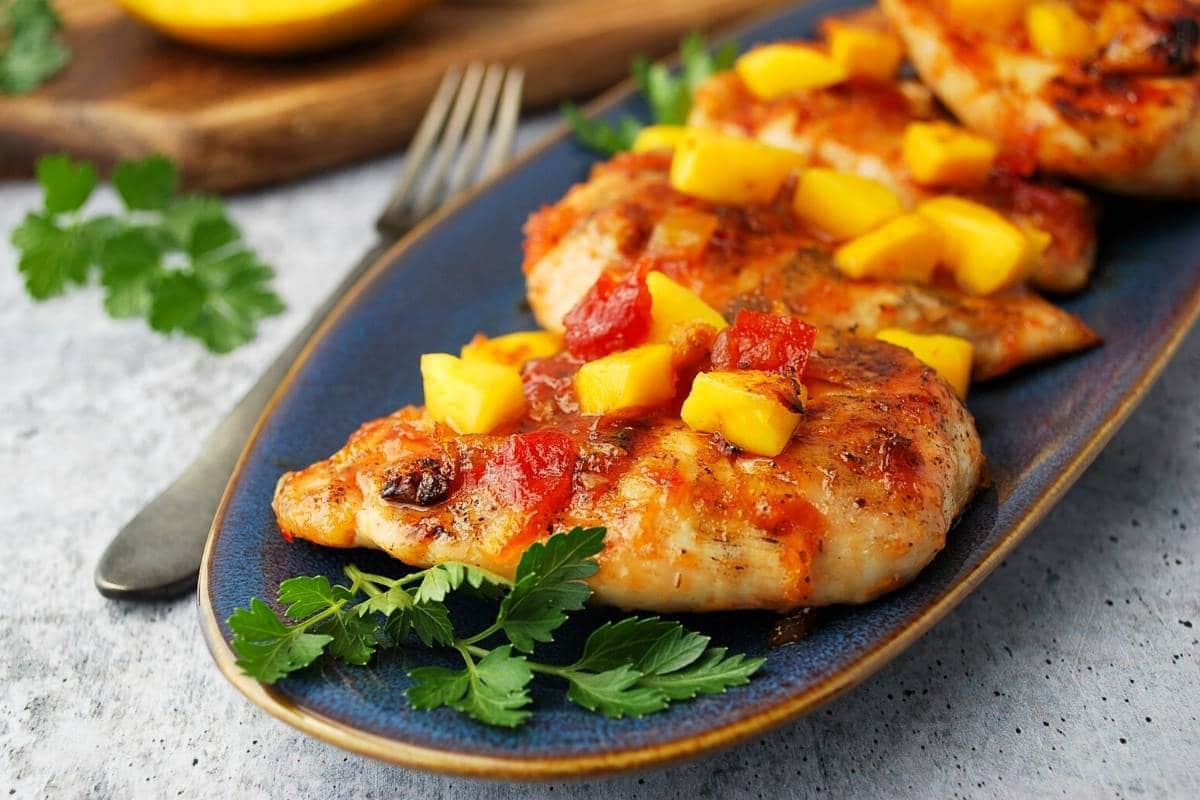 side view of grilled mango chicken on a platter with fresh parsley and a fork