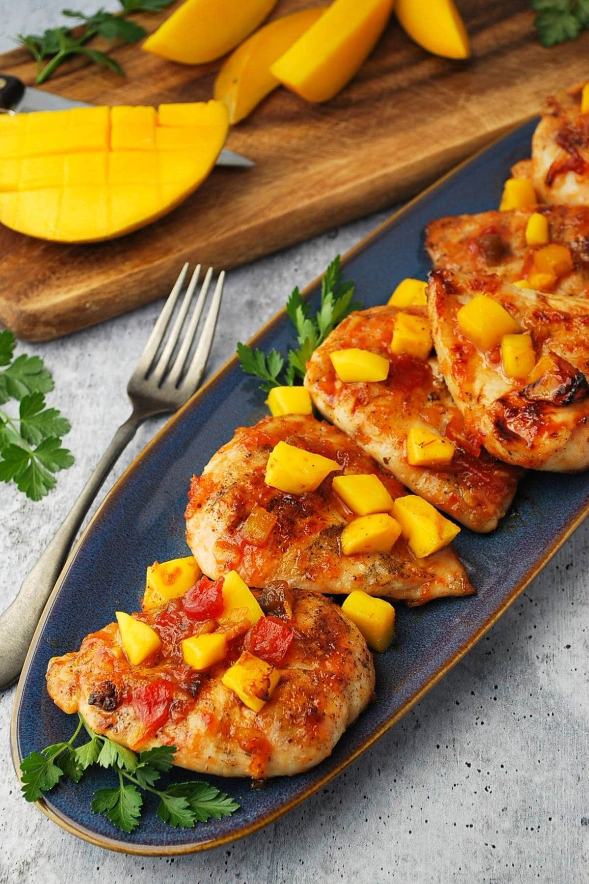 platter of grilled mango chicken with sliced fresh mango in the background