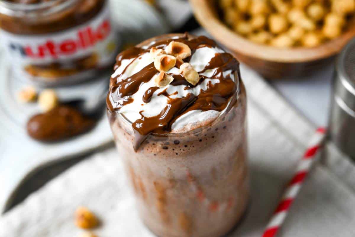 overhead photo of a protein shake drizzled with nutella and nuts with a spoonful of nutella next to it