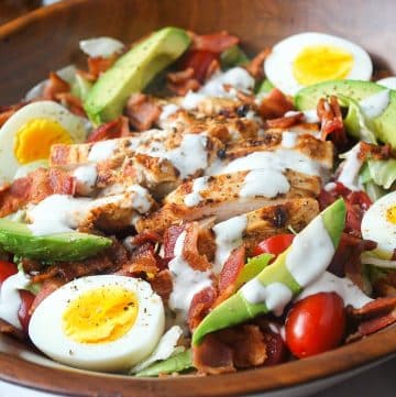 close up of a BLT salad with grilled chicken breast, hard boiled egg, avocado, tomatoes, and bacon in a wood bowl