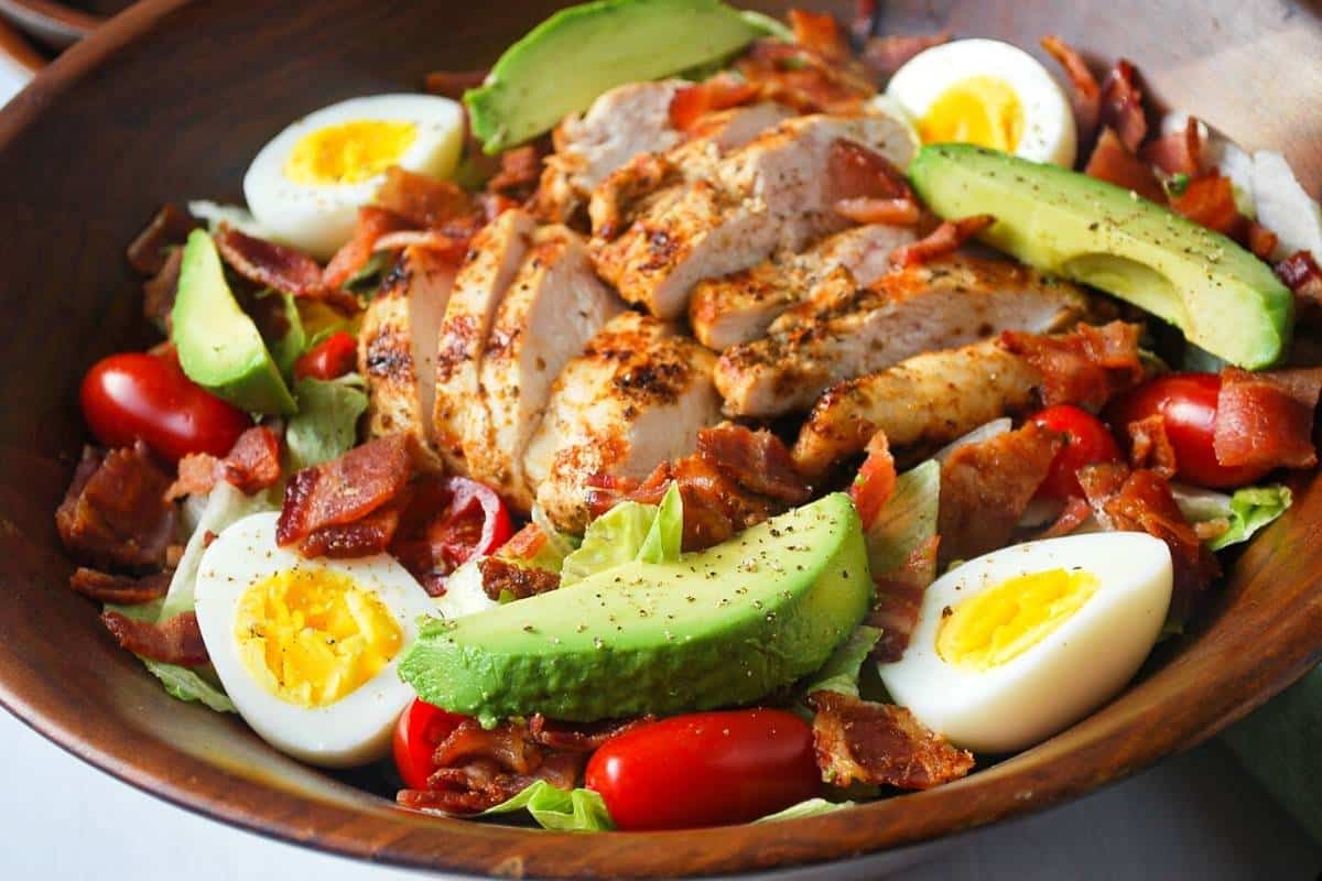 A bowl of salad with grilled chicken, bacon, eggs, and avocado on iceberg lettuce