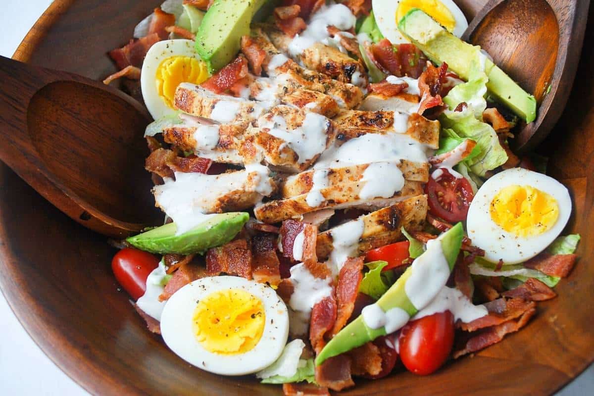 BLT chicken salad with a mayo vinaigrette on top with wooden salad serving utensils
