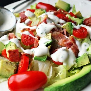 close up of a salad with tomatoes, avocados, bacon and ranch in a bowl