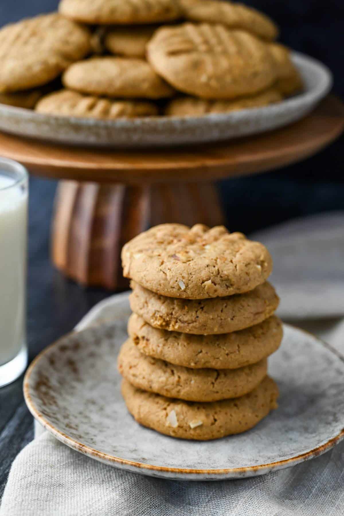 a plate of stacked cashew butter cookies with almonds with a platter of cookies behind it