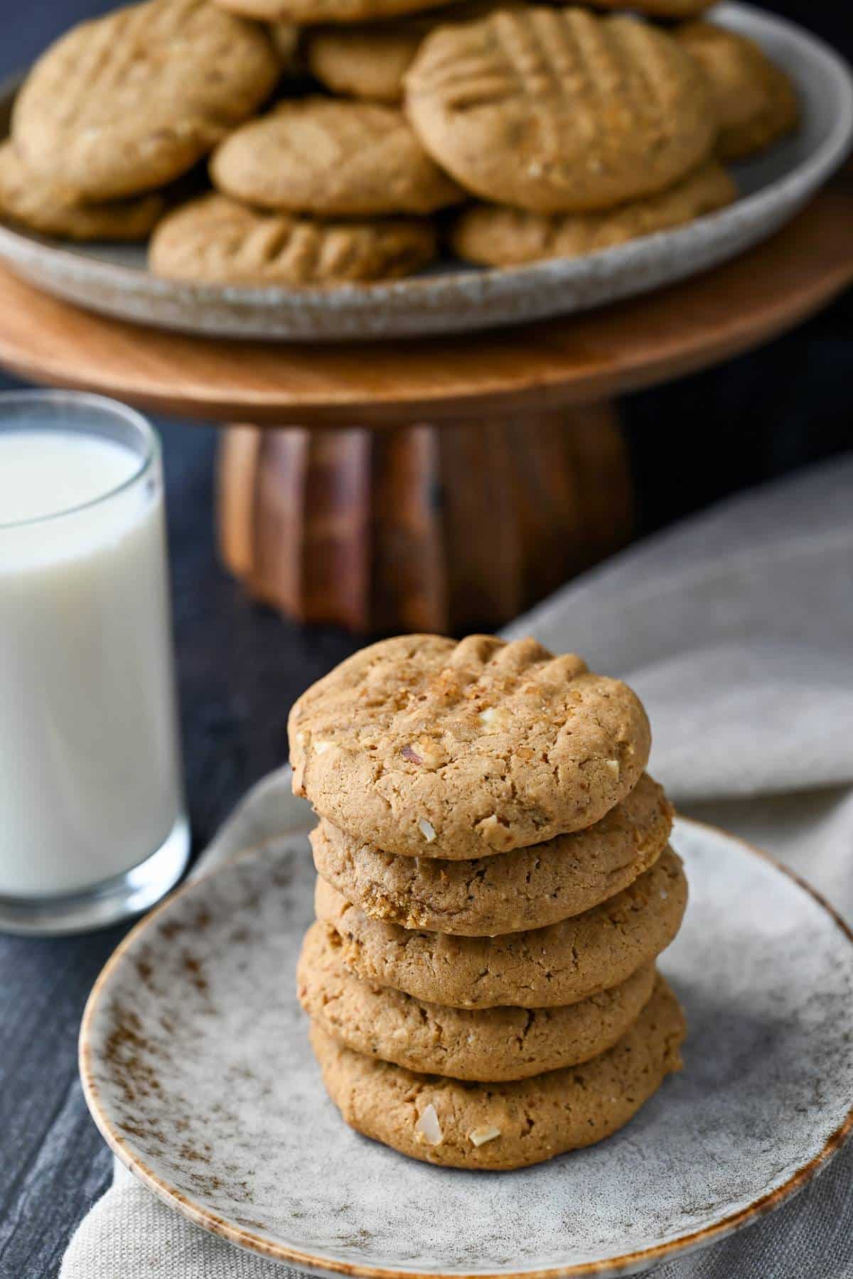 stacked cashew butter cookies on a plate with a napkin underneath and a glass of milk