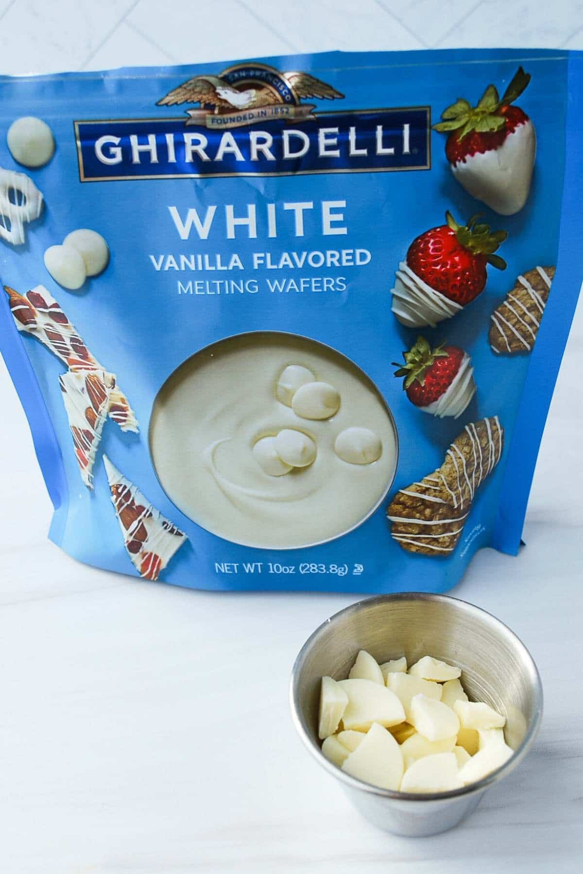 Ghiradelli white chocolate chips in a bag with a cup of chopped white chocolate