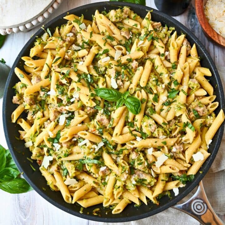 a skillet with zucchini pasta with sausage and fresh basil
