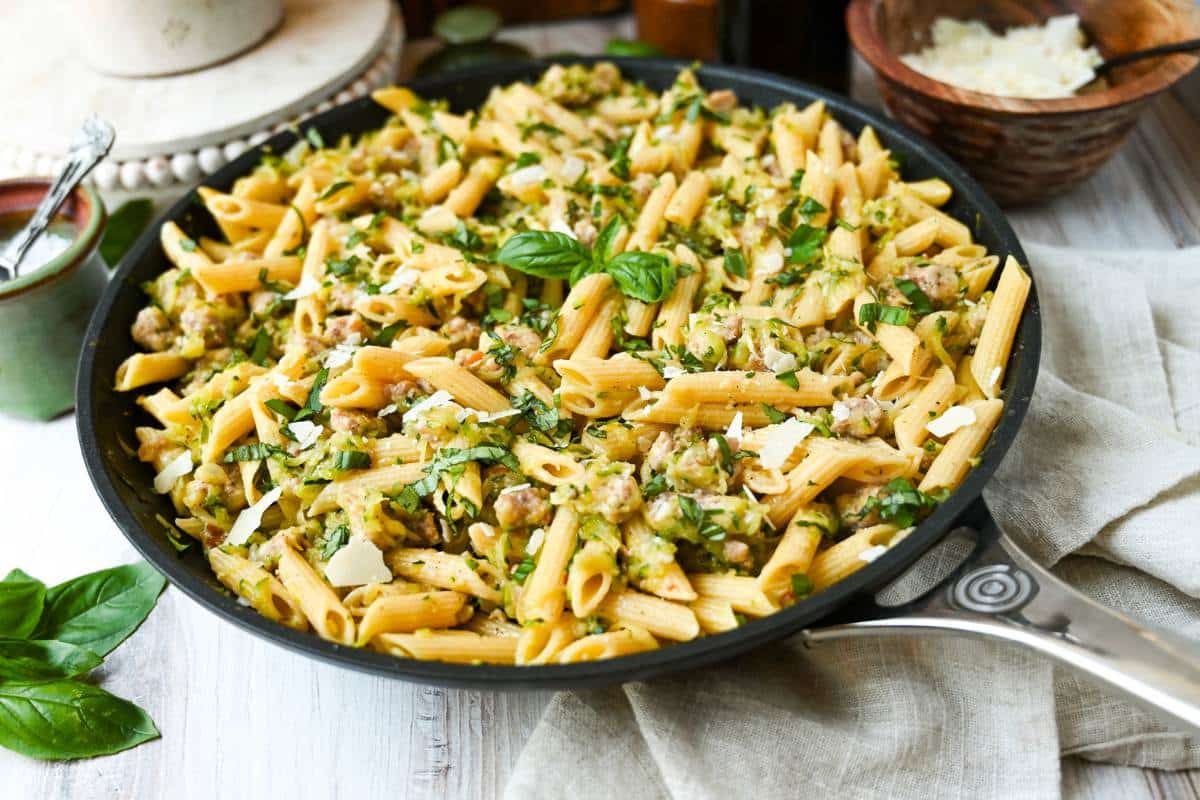 a pasta skillet with fresh basil and parmesan cheese next to it