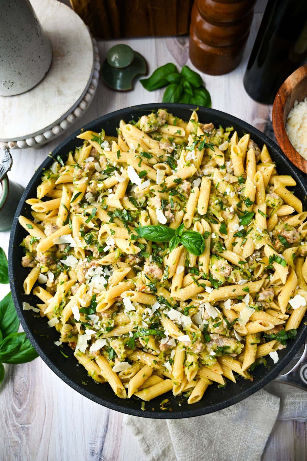 a large skillet of pasta with zucchini, sausage, basil, olive oil, and parmesan cheese