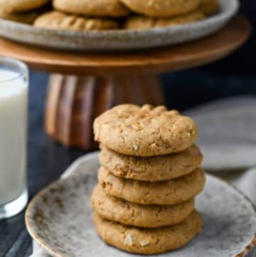a stack of cookies on a small plate with a wood platter of cookies behind it