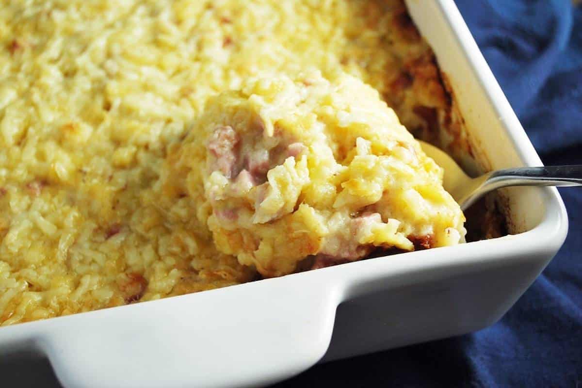 A spoon dipping into a casserole dish of hashbrown casserole made with gluten free soup
