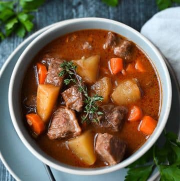 a bowl of beef stew with fresh thyme a spoon and a napkin