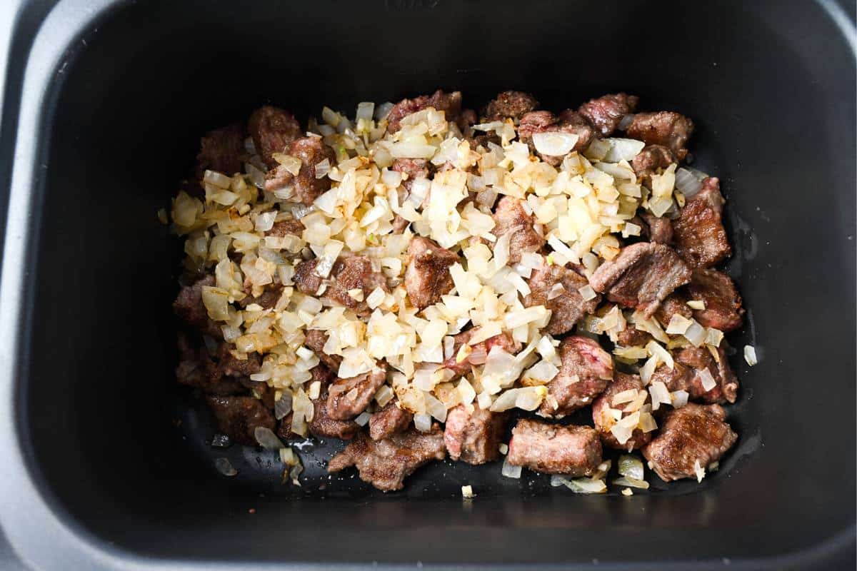 seared beef and sauteed onions and garlic in a slow cooker
