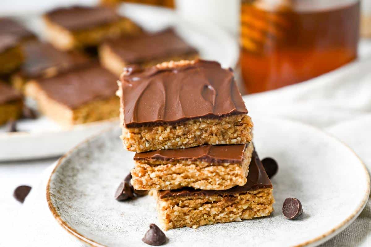 stacked dessert bars on a plate with a jar of honey and platter of bars behind it