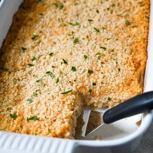 chicken hashbrown casserole in a white baking dish with a serving cut out of it
