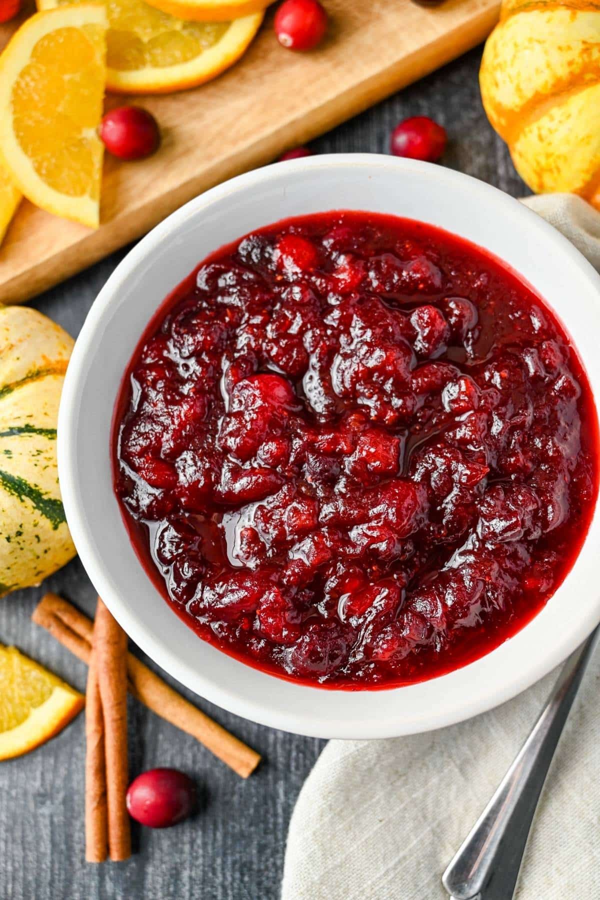 a bowl of cranberry sauce with sliced oranges, cinnamon sticks and cranberries around it