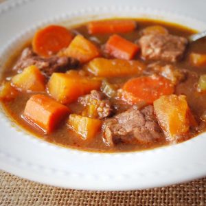 close up of a bowl of beef stew with sweet potatoes and carrots with a spoon