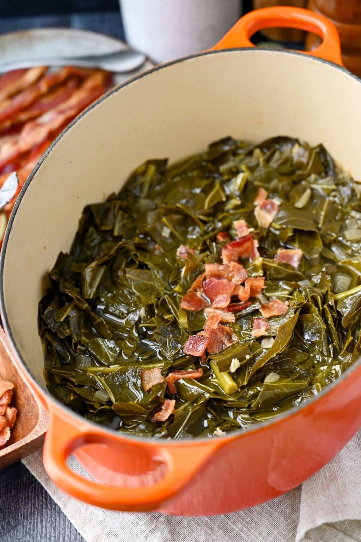 side view of a pot of braised collard greens with bacon on top