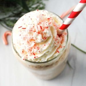 overhead photo of a peppermint protein shake in a glass with striped straw, whipped cream, and candy canes