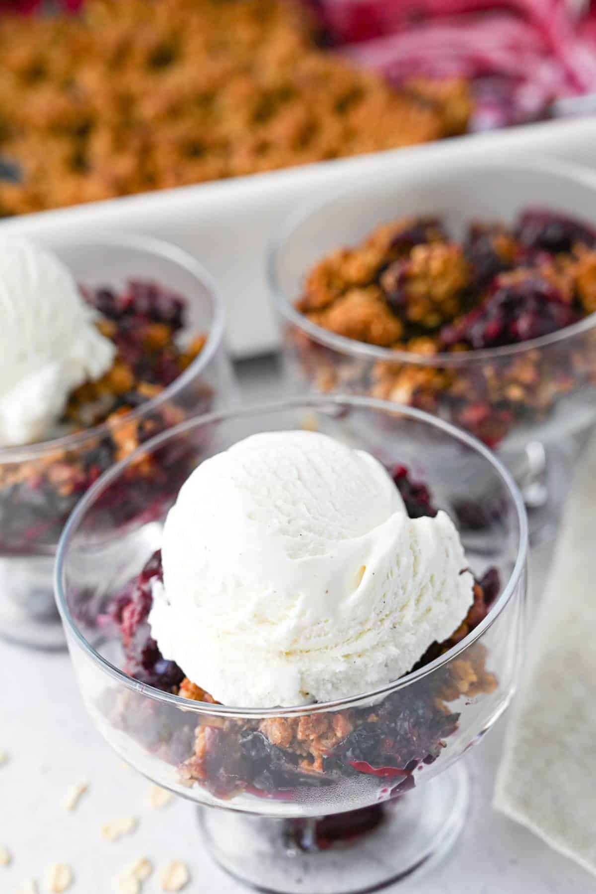 berry crisp in dessert dishes with a pan of crisp in the background