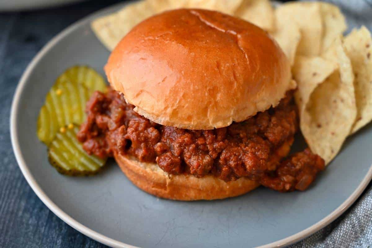 side view of venison sloppy joe meat on a brioche bun with corn chips and pickles