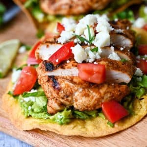 close up of an avocado tostada topped with grilled chicken, lettuce, tomatoes, queso fresco cheese and cilantro