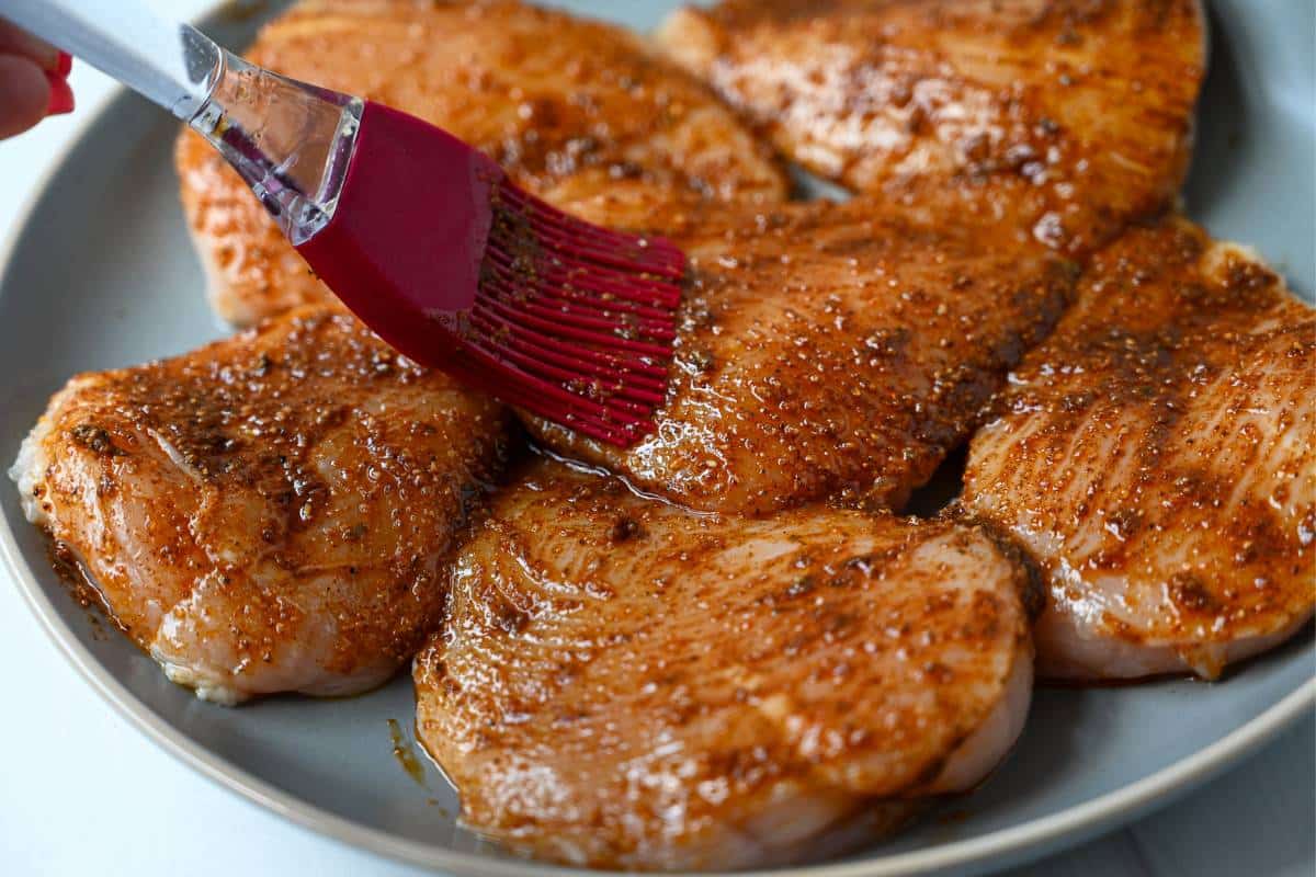 brushing a marinade rub on chicken breasts