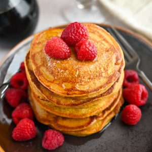 an close up photo of a tall stack of pumpkin protein pancakes with raspberries and drippy syrup