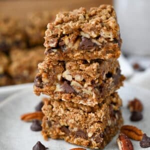 a stack of carmelita bars on a plate with pecans and chocolate chips