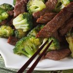 beef and broccoli on a plate with chopsticks
