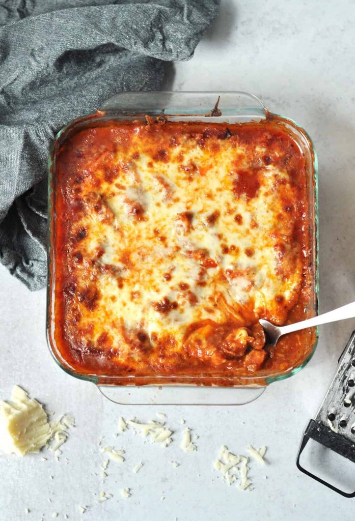 casserole topped with tomato sauce and cheese in a pan with a serving spoon