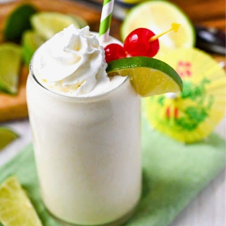 a banana pineapple protein shake with whipped cream, cherries and a lime wedge
