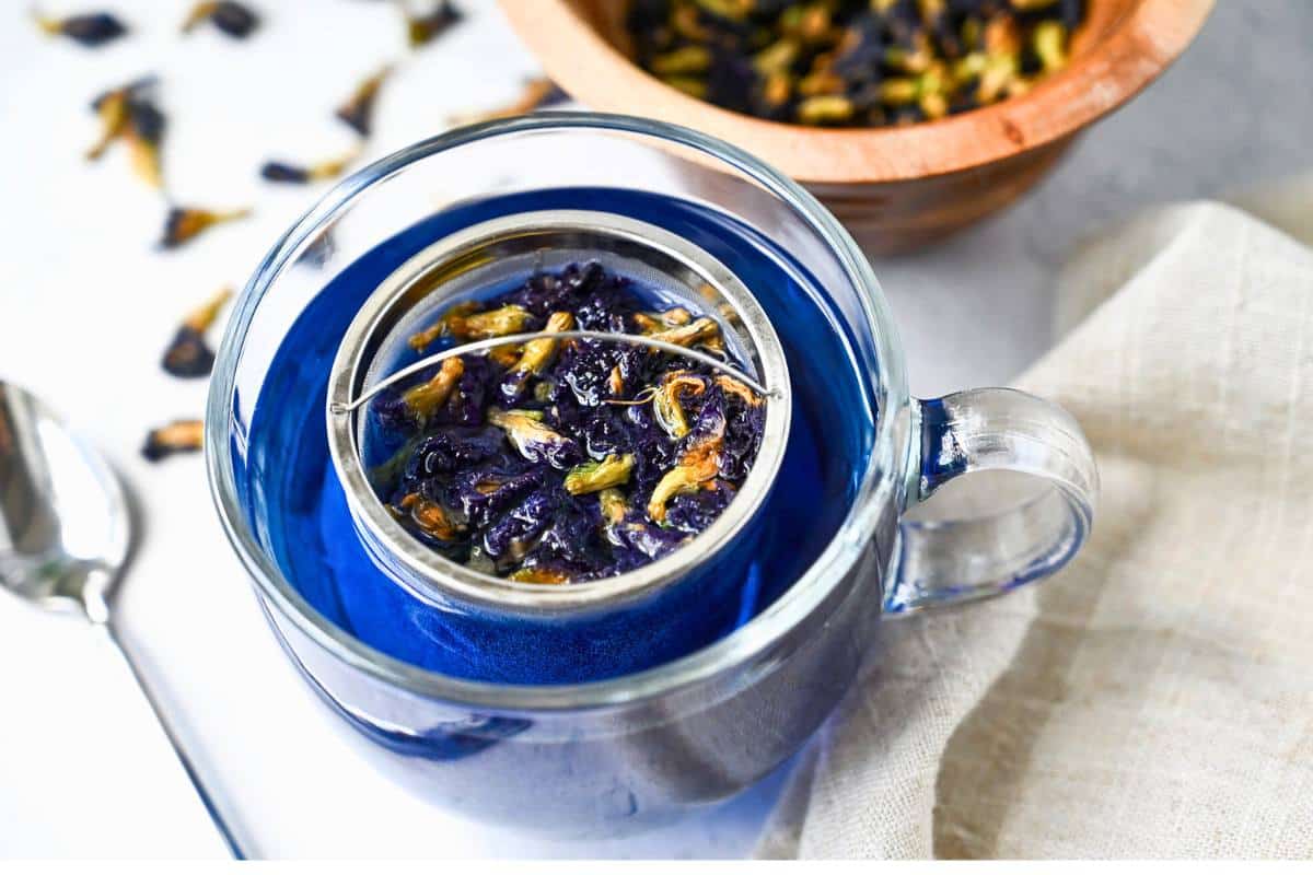 a clear glass mug with steeping butterfly pea flowers and a bowl full of dried butterfly pea flowers