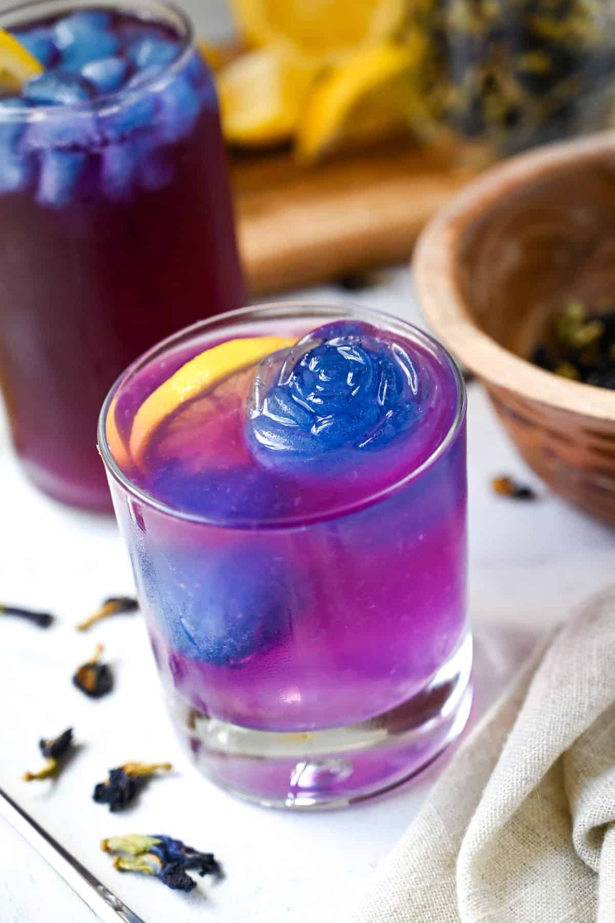 purple butterfly pea flower lemonade in two glasses garnished with lemon 
