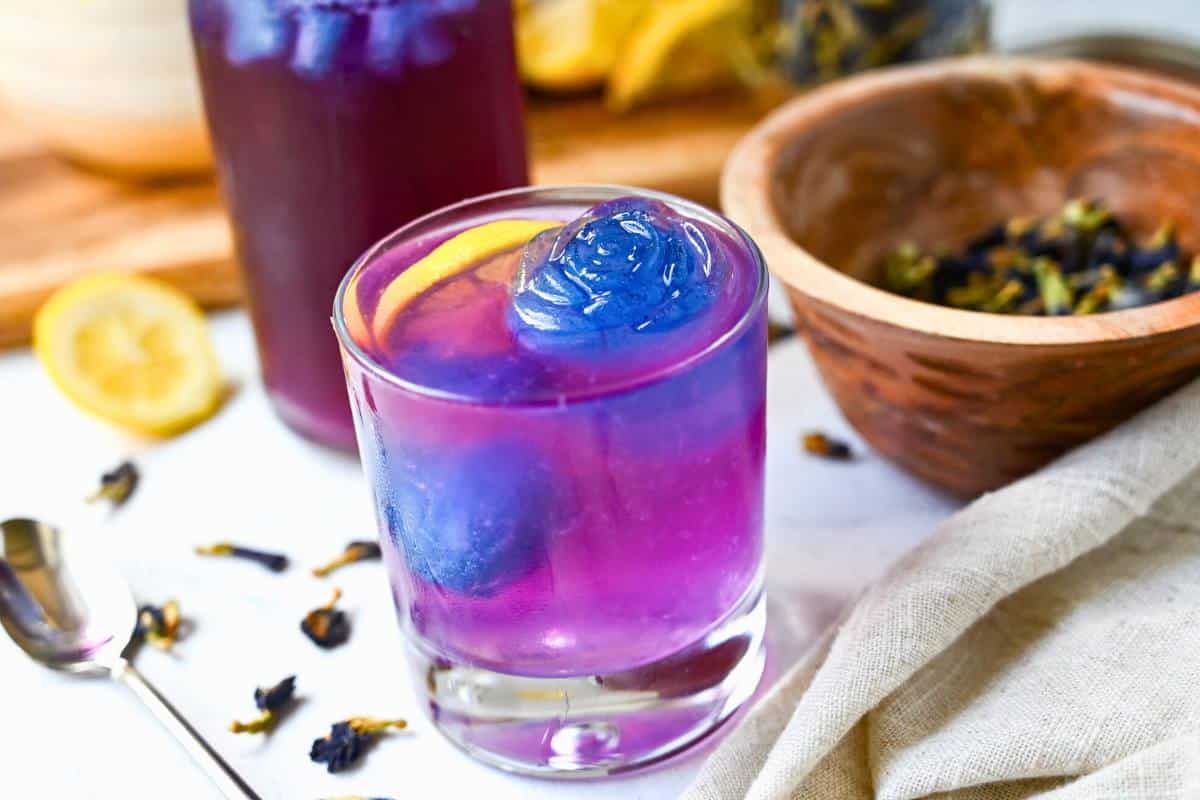 a low ball glass with rose ice cubes with purple lemonade made with lemon juice and butterfly pea flower tea