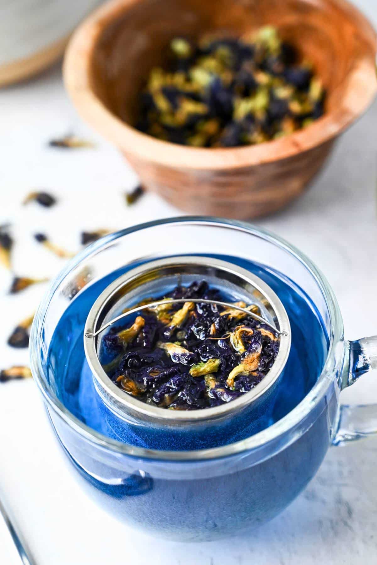 butterfly pea flower blossoms steeping in a glass mug in a tea strainer