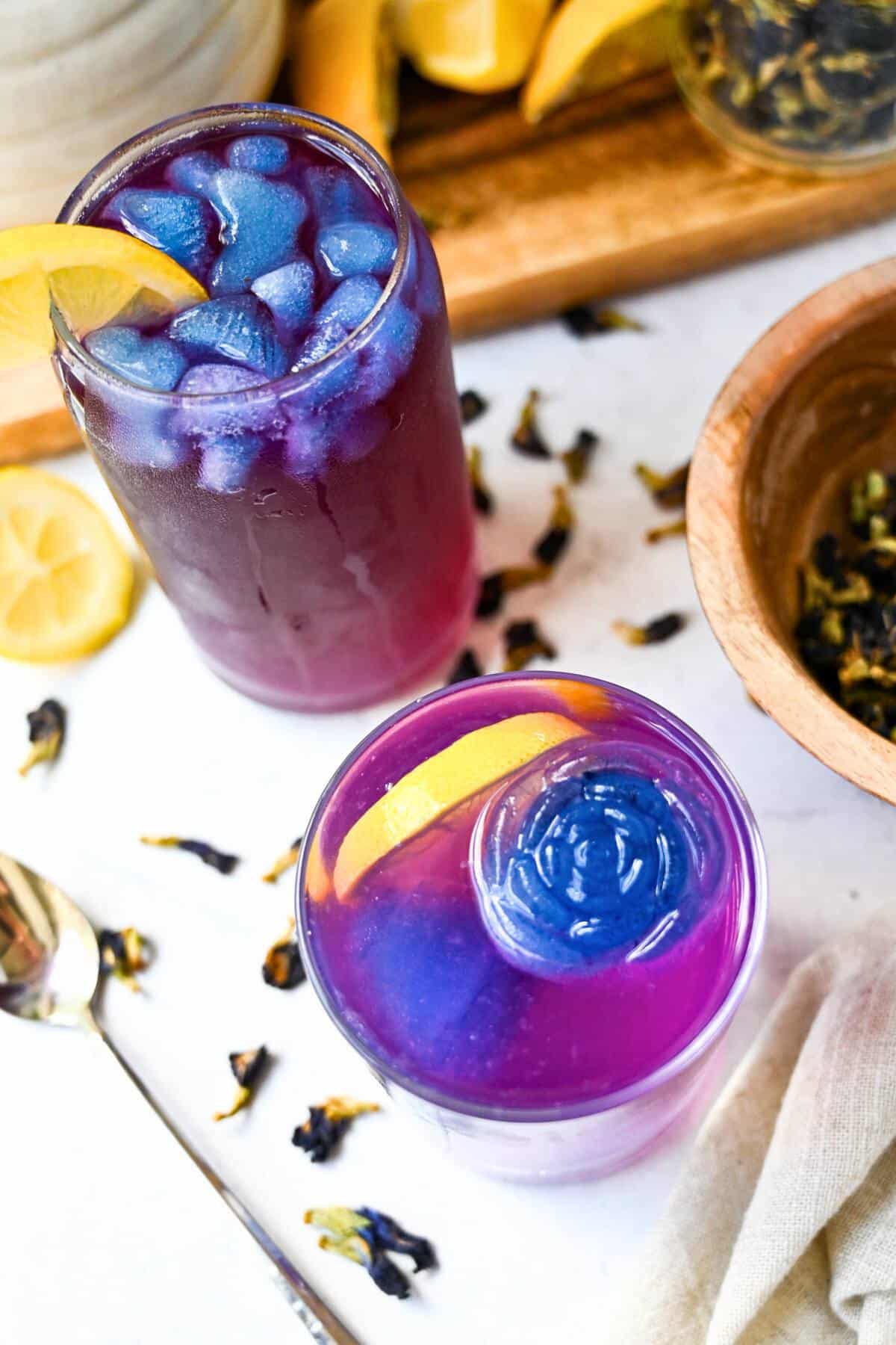 two glasses of butterfly pea flower lemonade with lemon wedges and a spoon