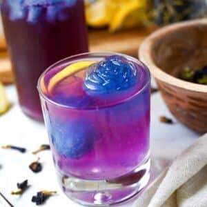close up of a glass of purple lemonade with a large rose shaped blue ice cube