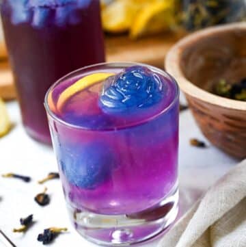 close up of a glass of purple lemonade with a large rose shaped blue ice cube