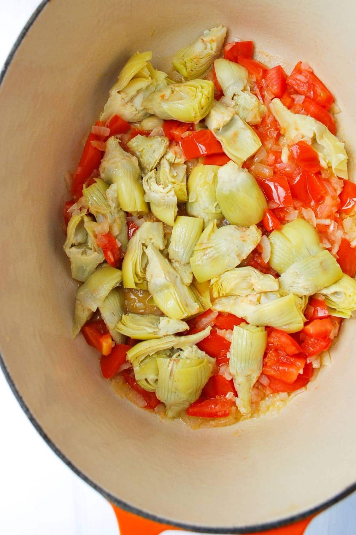 artichokes, tomatoes, and onion sauteing in a dutch oven