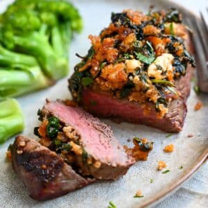 a sliced mediterranean steak on a plate with a fork and steamed broccoli