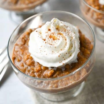 a photo of oat milk rice pudding in a glass parfait dish with whipped cream and cinnamon on top