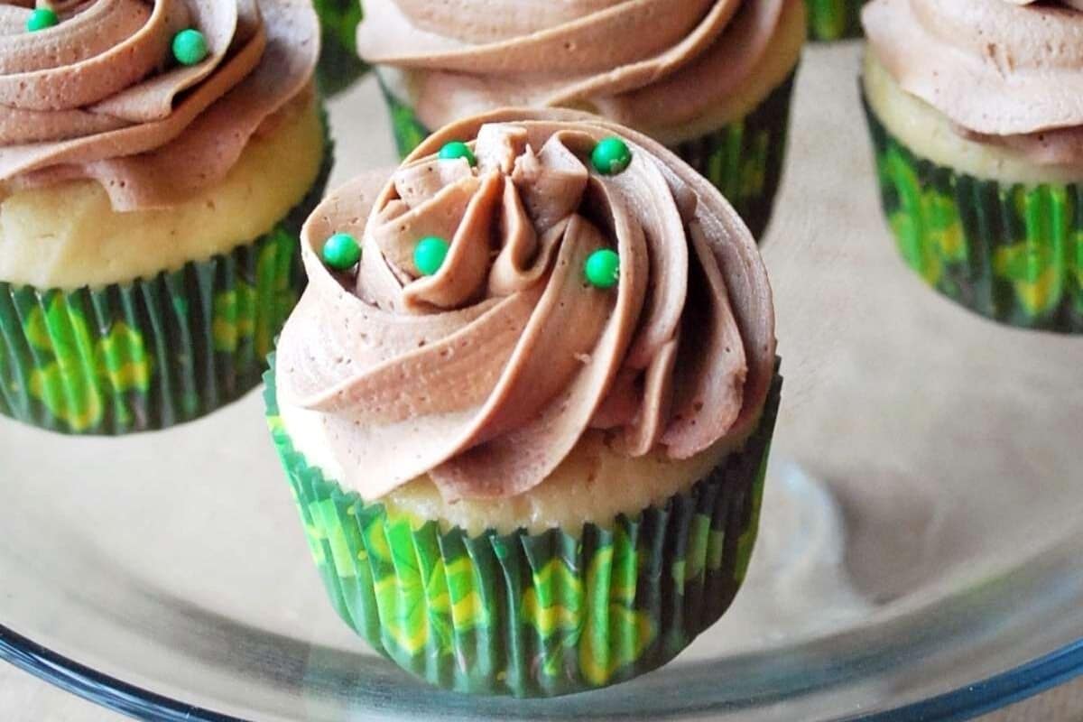 Bailey's cupcakes with mocha frosting and green sprinkles on a glass cake stand