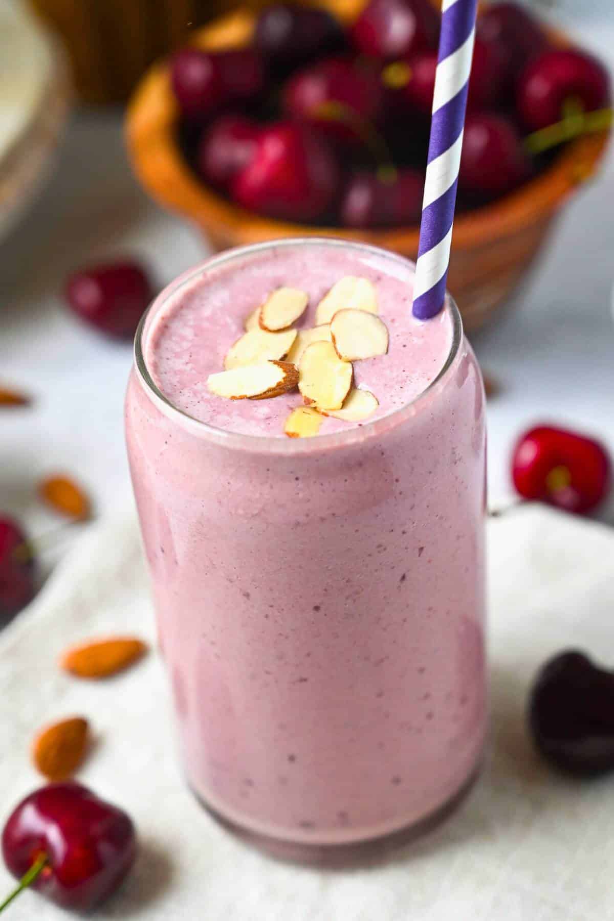 close up of a cherry almond smoothie in a glass with cherries and almonds around it