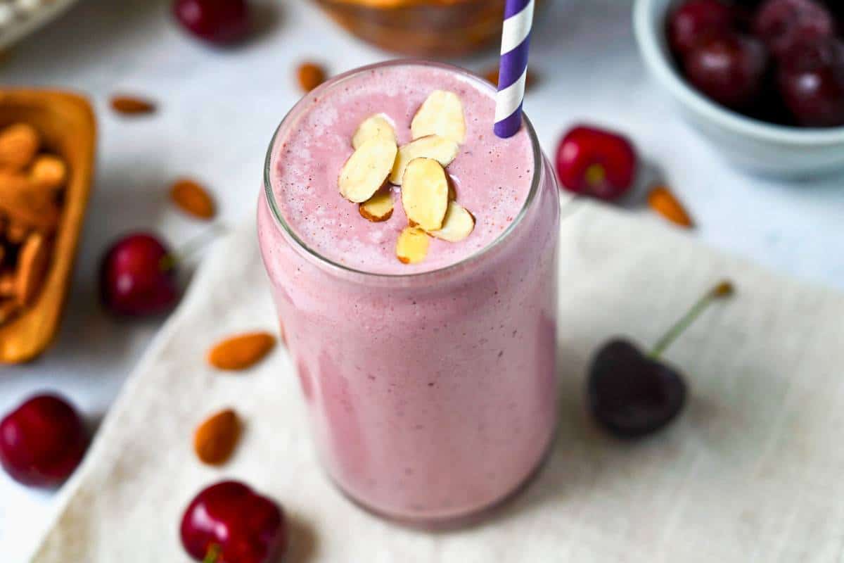 looking down at a cherry smoothie with almonds on top with whole cherries and almonds around it